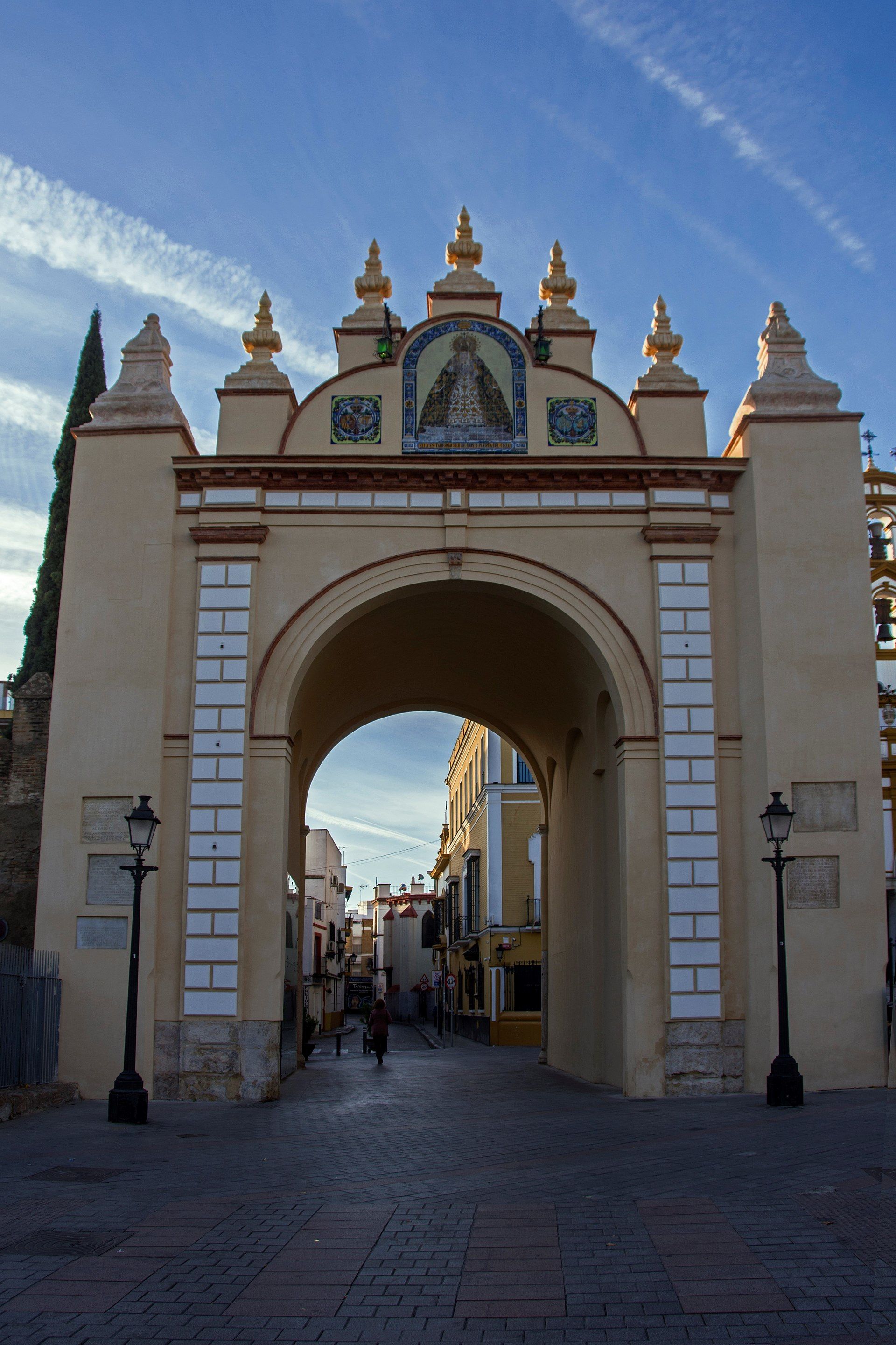 Arco de la Macarena en Sevilla con un mosaico de la Virgen en la parte superior, bajo un cielo azul.