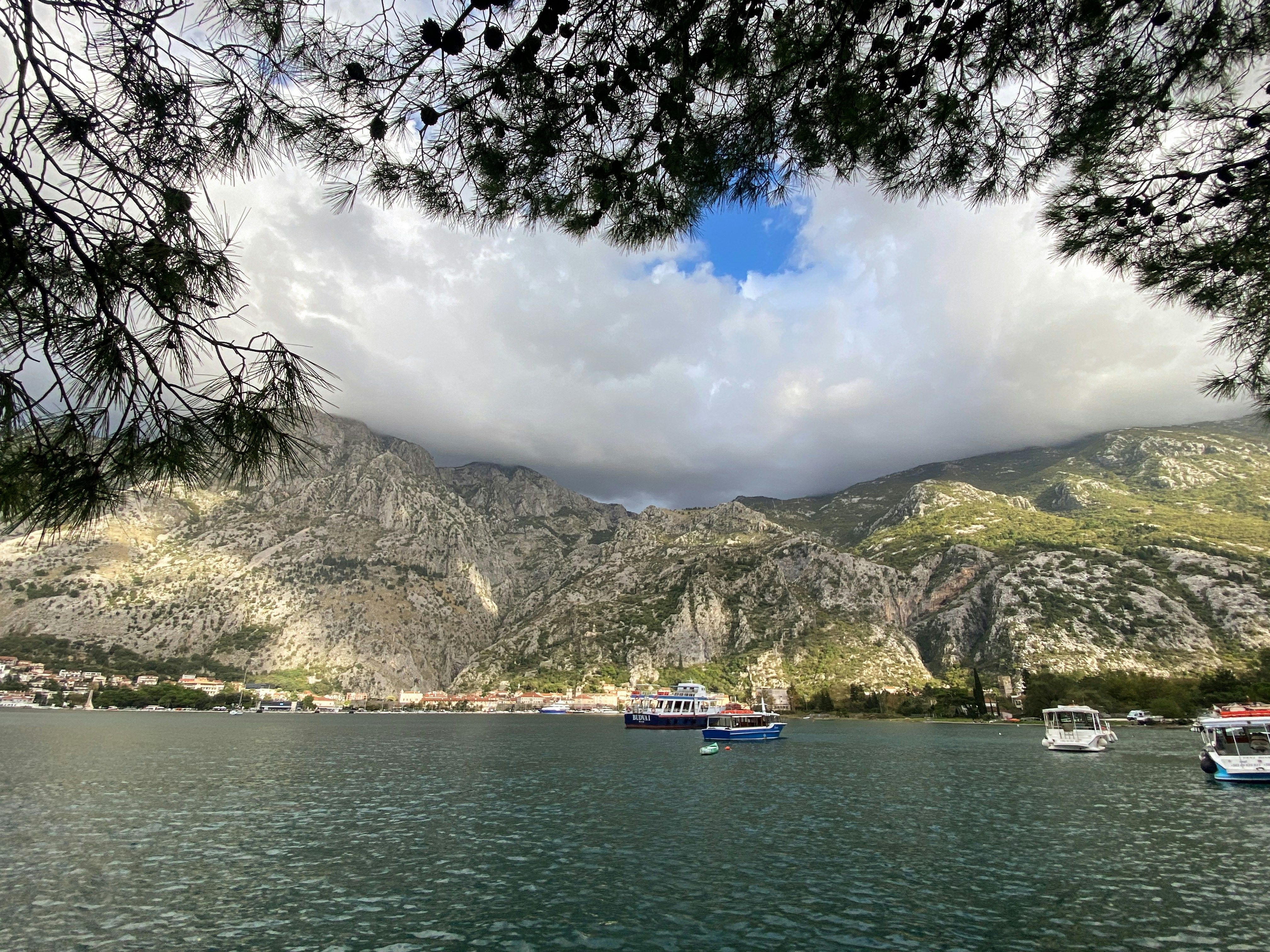 Vista panorámica de un lago con montañas rocosas y un pueblo costero bajo un cielo nublado.