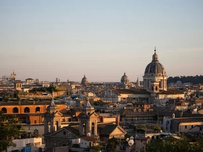 Vista panorámica de Roma al atardecer, con cúpulas de iglesias y edificios antiguos bajo un cielo azul rosado
