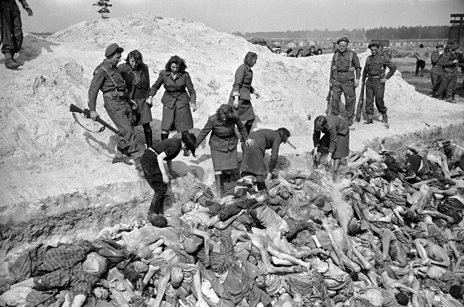 Guardianas de las SS del campo de concentración de Bergen-Belsen descargan cadáveres de prisioneros para enterrarlos en una fosa común. Fueron reclutadas para este trabajo por los Aliados que liberaron el campo. Un convoy de soldados británicos rodea la zanja. A las antiguas guardianas se las castiga prohibiéndoles usar guantes, lo que las expone al riesgo de contraer tifus. En la imagen