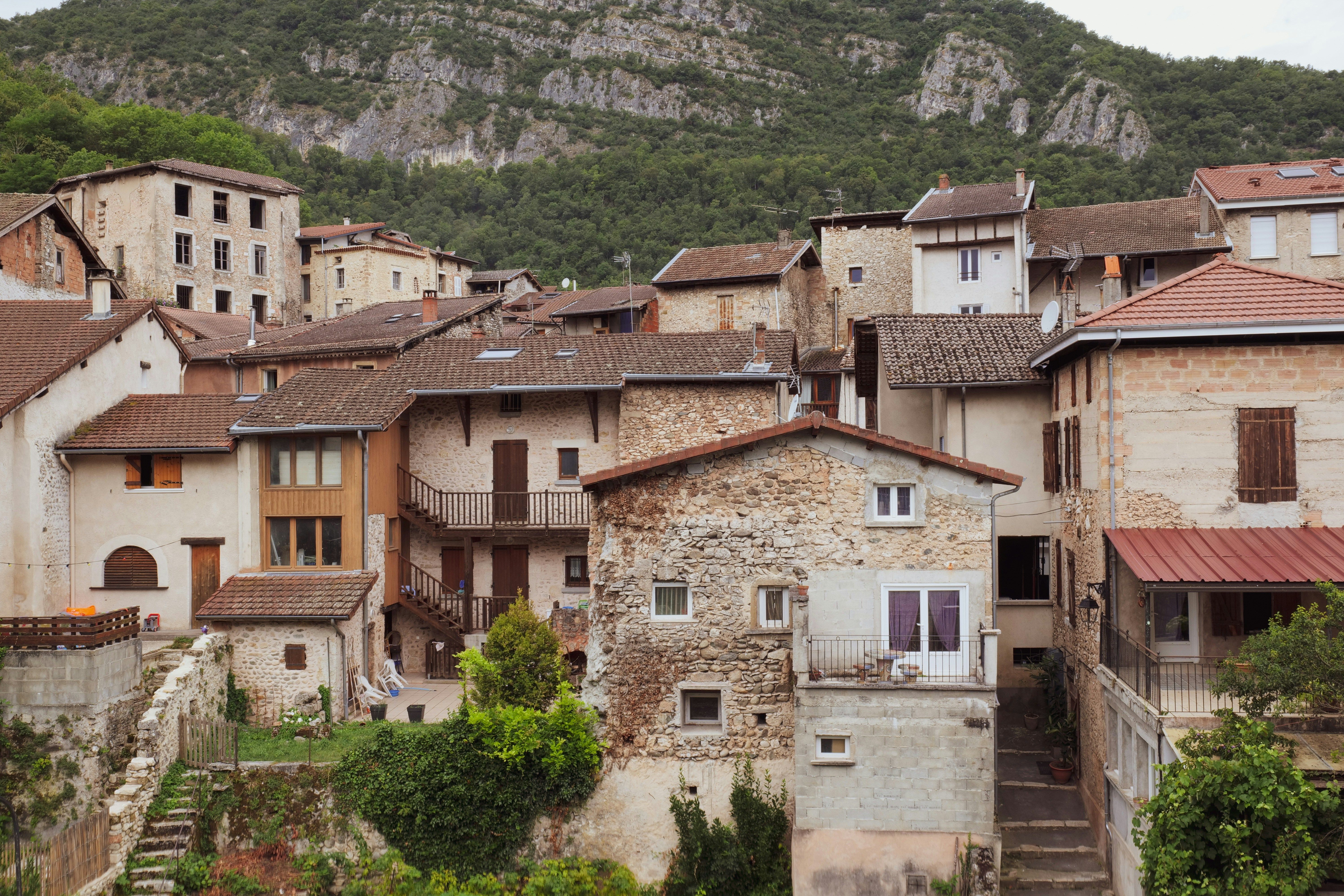 Vista de un pueblo de montaña con casas de piedra y tejados de teja, rodeado de vegetación y montañas.