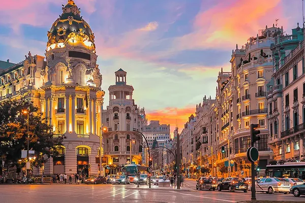 Vista del Edificio Metrópolis en Madrid al atardecer, con cúpula iluminada, fachadas ornamentadas y calles con tráfico