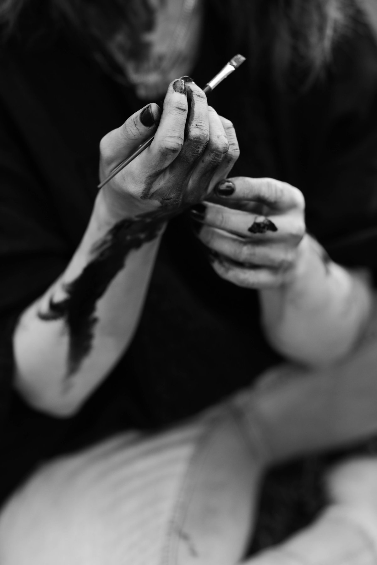 Close on two paint-covered hands, one holding a brush, the face above them out of focus.