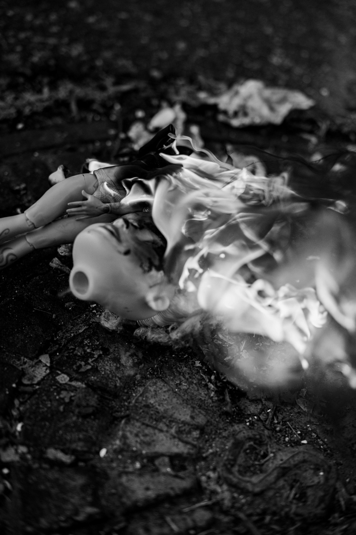 A doll lies on the ground engulfed in white flame, its body melting.