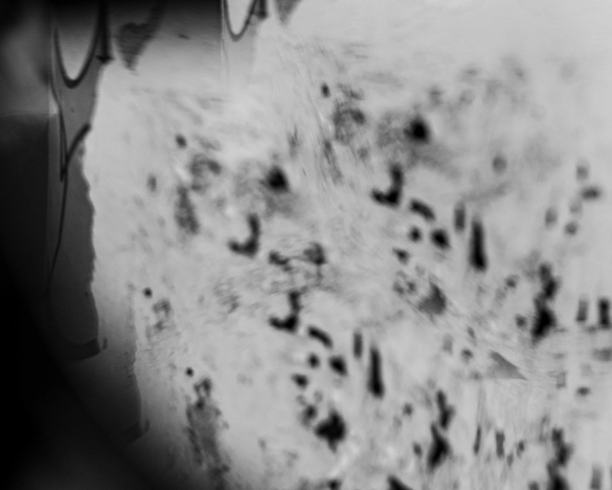 A blurred white wall spattered with dark marks, seen through a vignette.