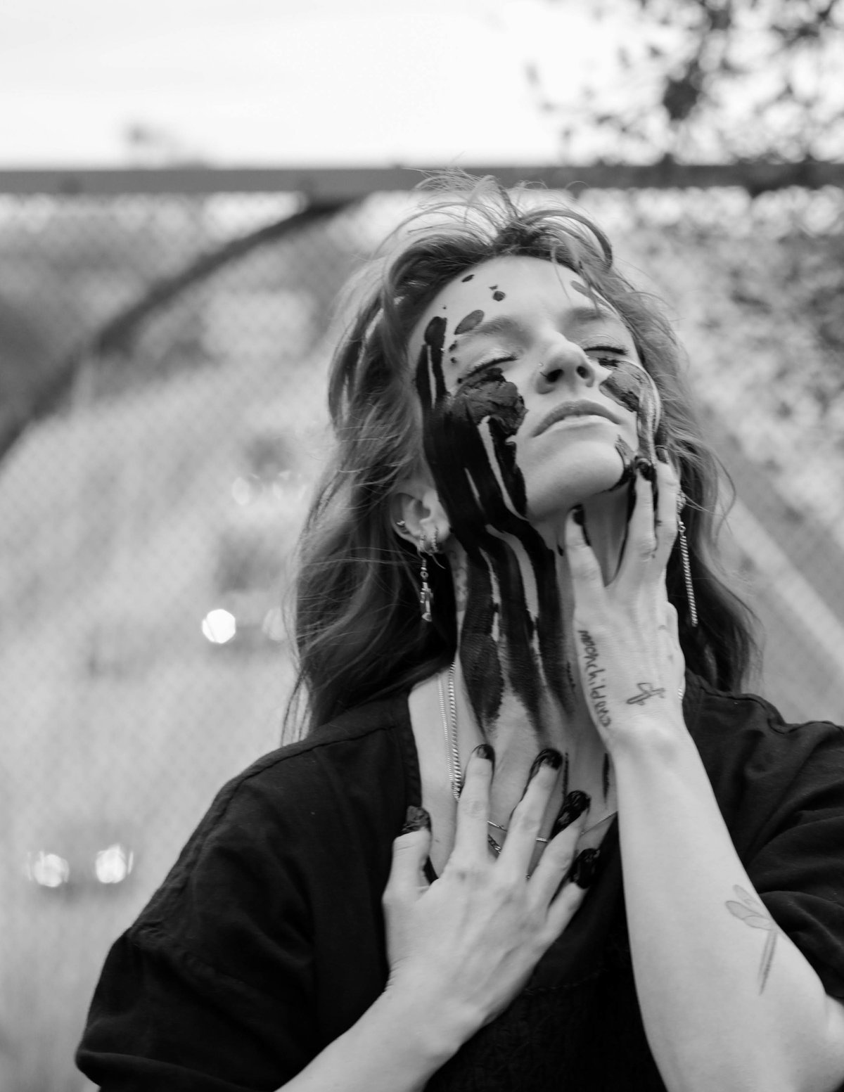 Eyes closed, face lifted, a woman with black paint streaming down her face presses her hands to her throat and chest.