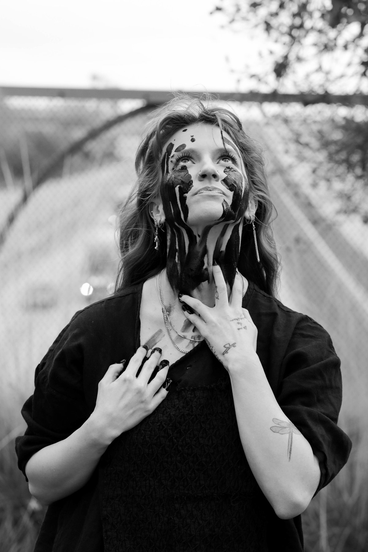 A woman gazes upward, black paint streaming from her eyes down her face and throat.