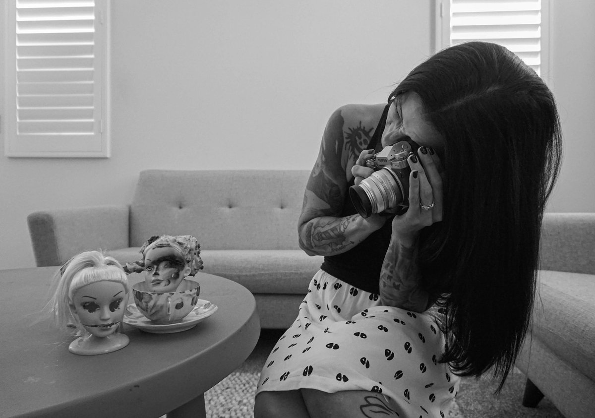A woman photographs two doll heads set up at a small table, one inside a teacup.