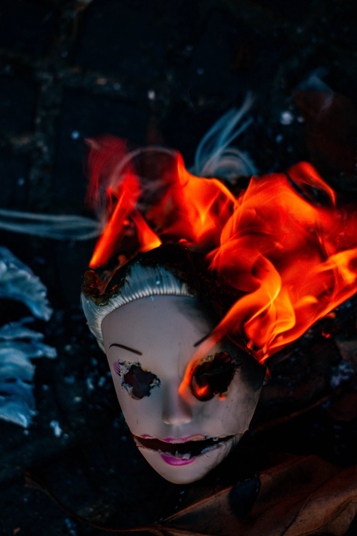 A doll's head with burned-out eyes, bright orange flames rising from its hair.