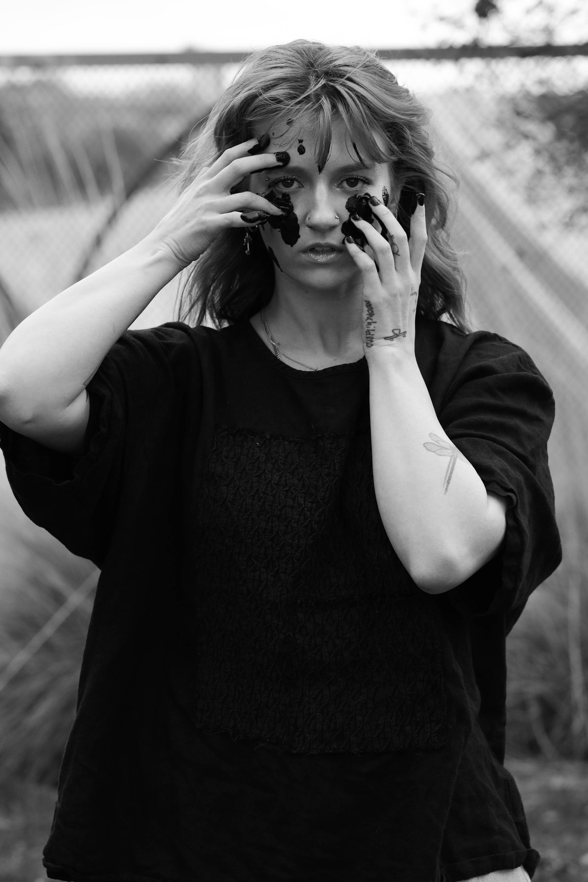 A woman looks into the camera, both hands pressed to her face, black paint smeared under her eyes.