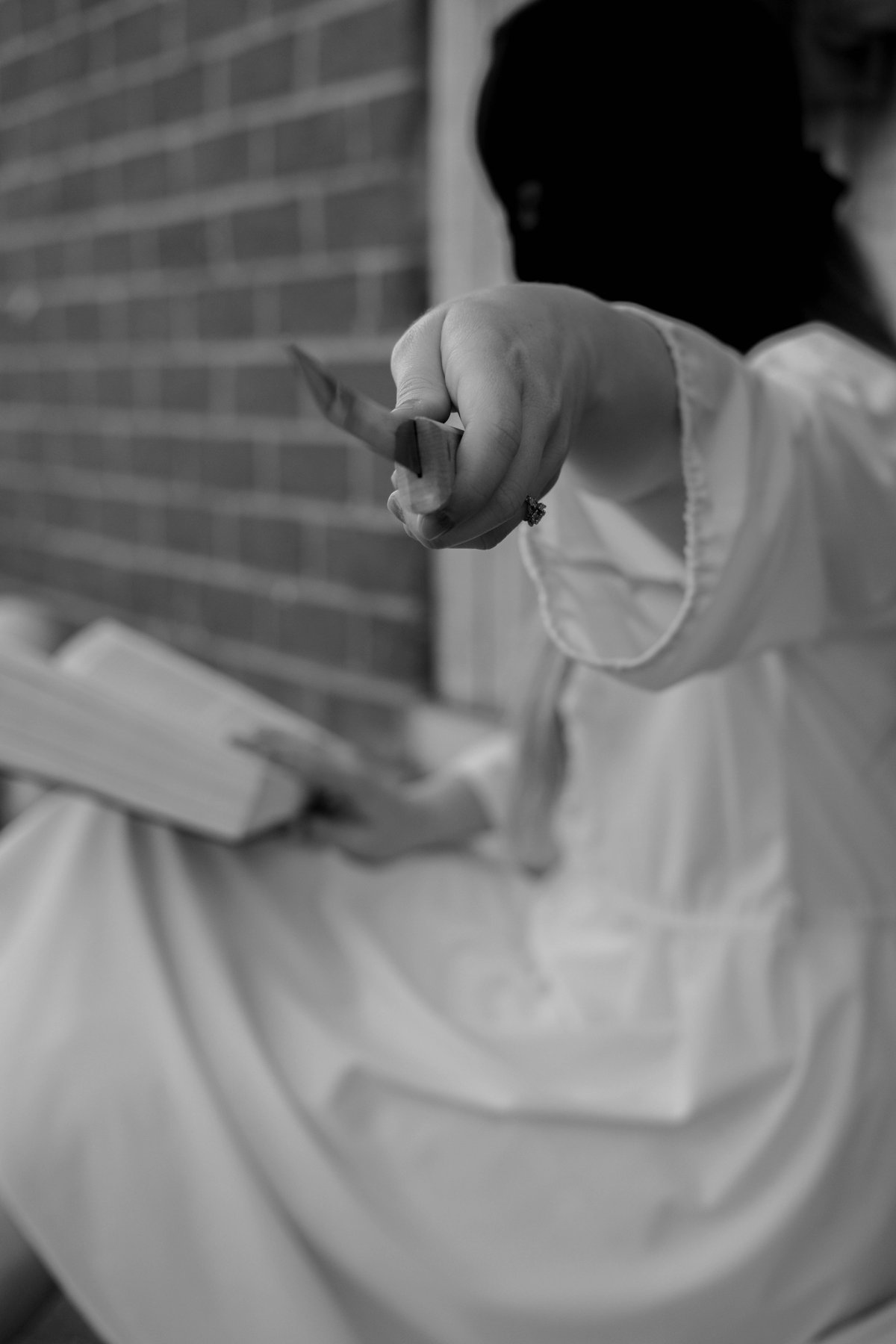 A masked woman holds a knife out toward the camera, a book open in her lap.