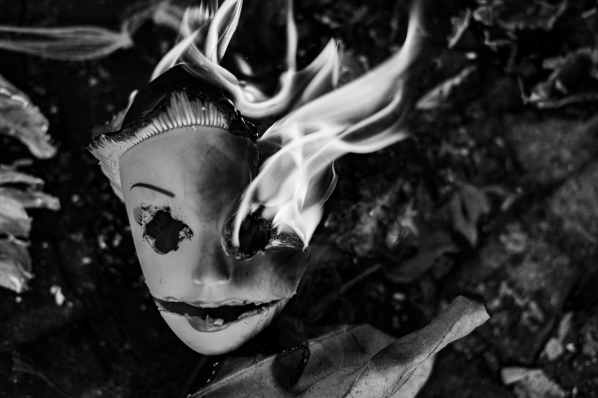 A doll's face burning on the ground, white flames rising from one eye.