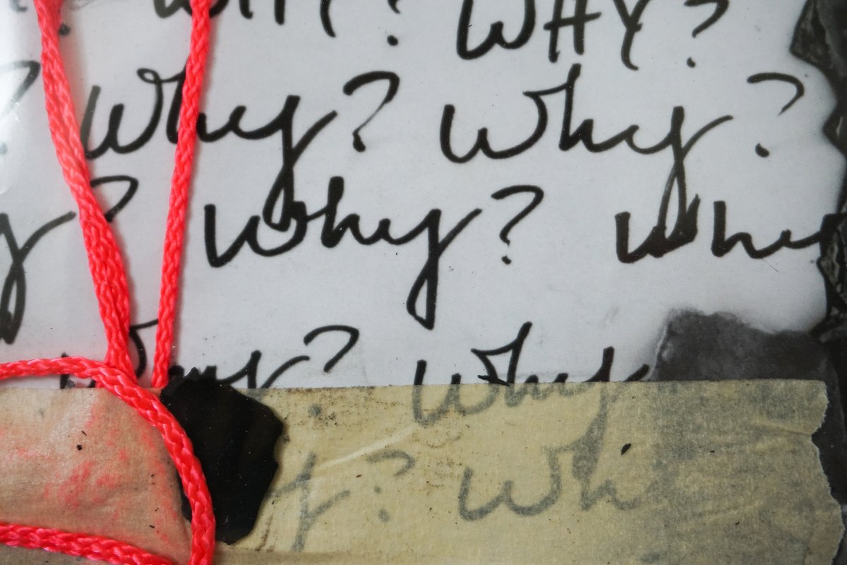 Close detail: handwritten 'Why?' above a strip of masking tape, a red string looping down over a charred scrap.