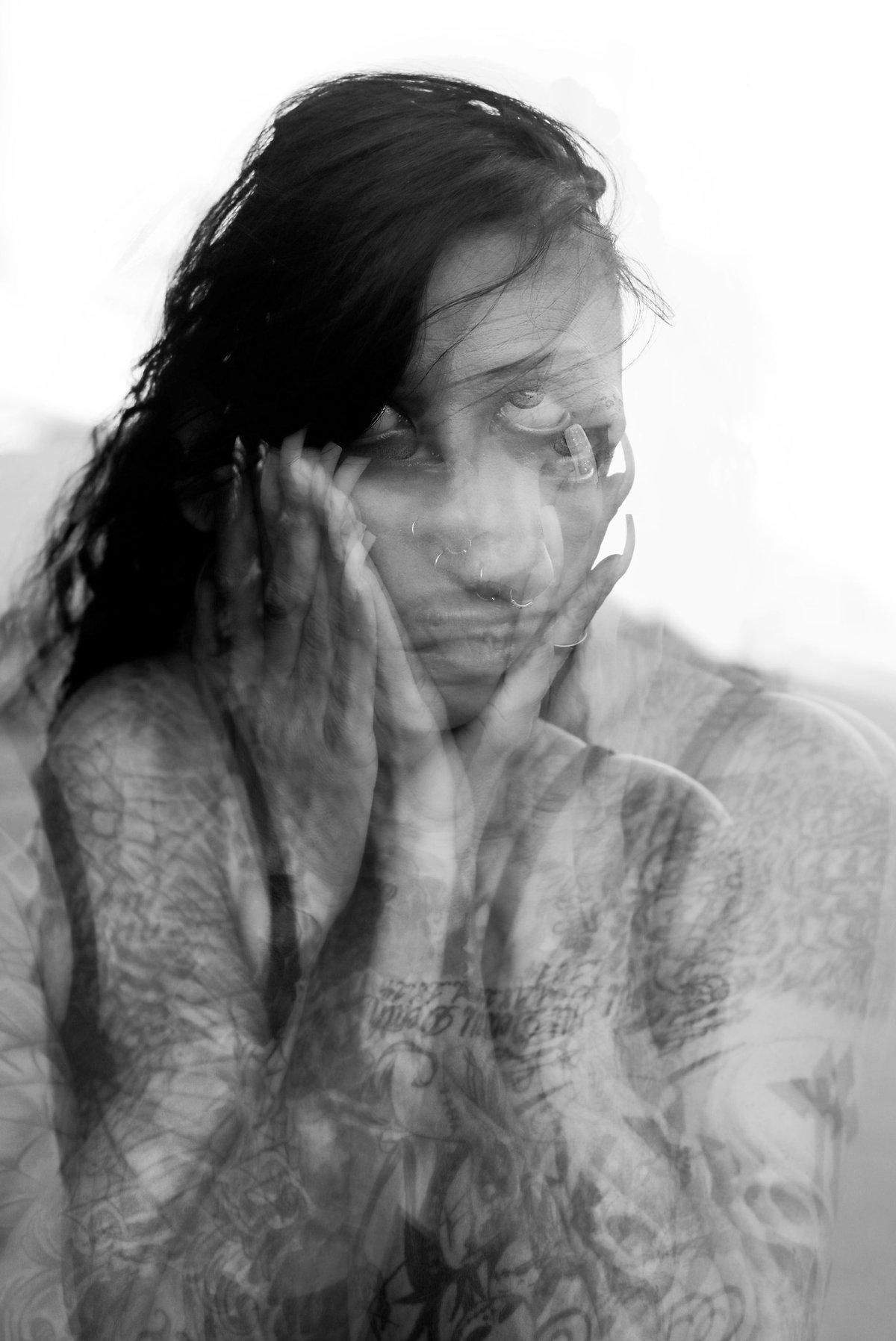 A woman holds her face in her hands, her image layered over itself in a ghostly double exposure.