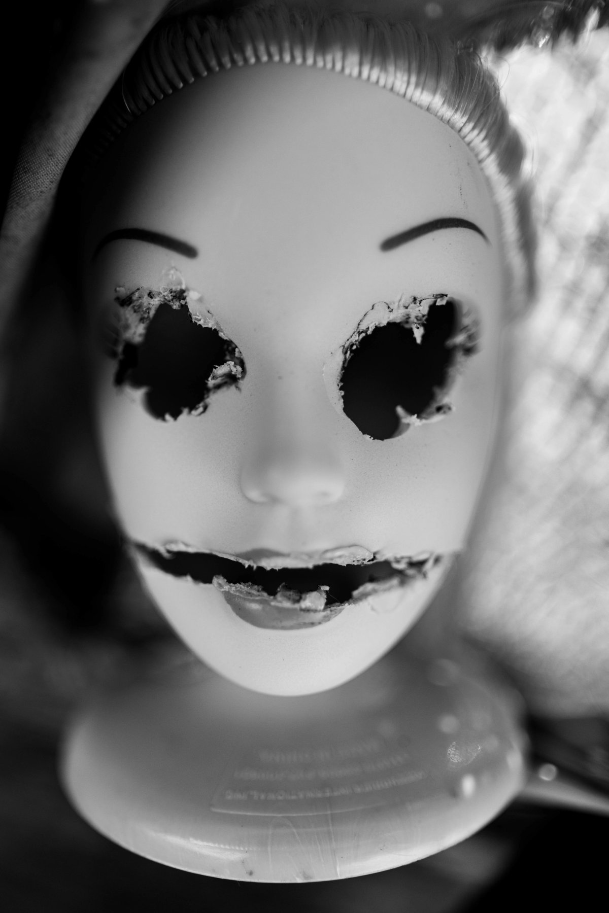 A doll head on a stand with burned-out eyes and a melted, grinning mouth.