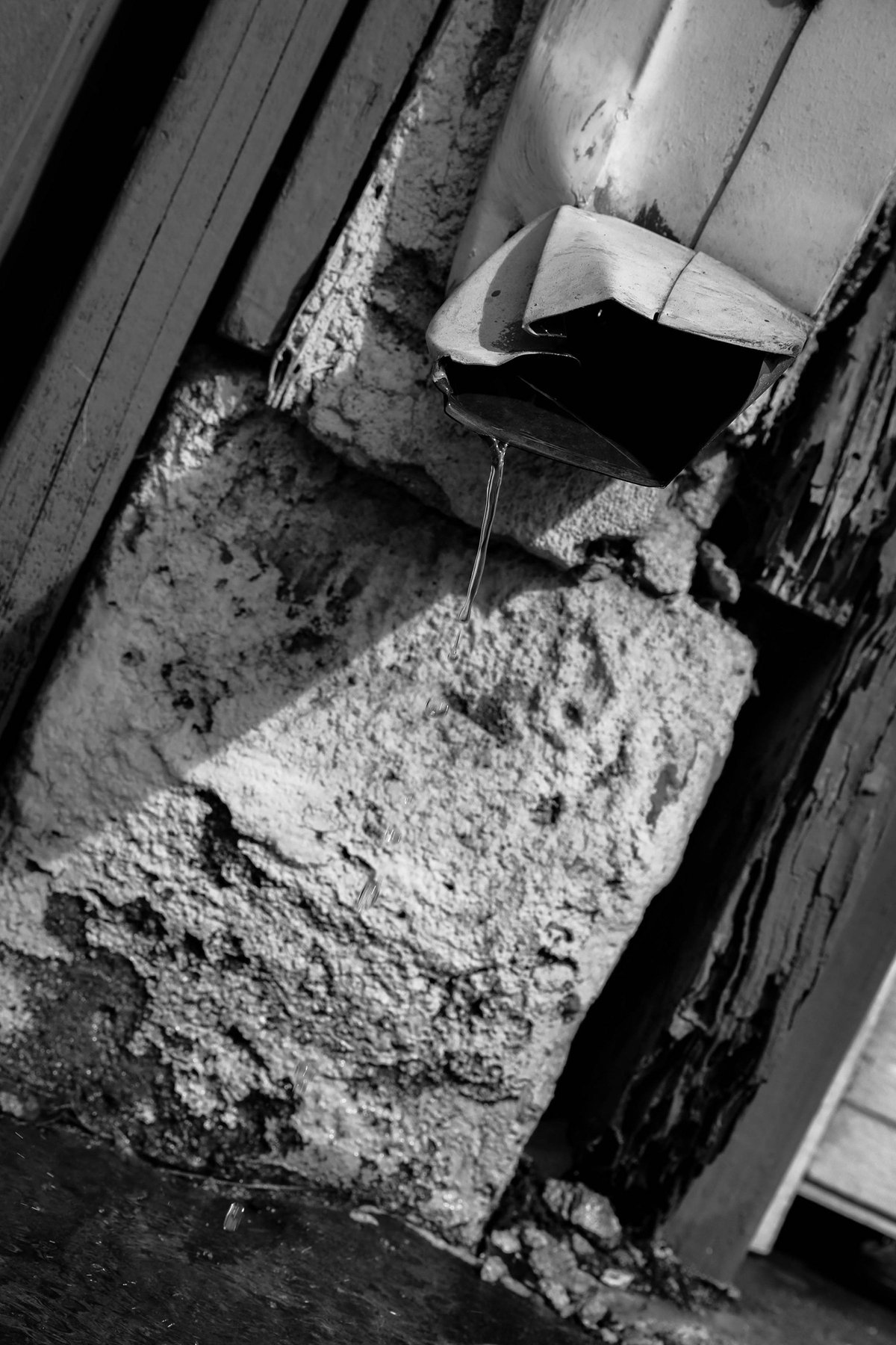 A crumpled black box wedged into a broken concrete corner, water dripping from it.