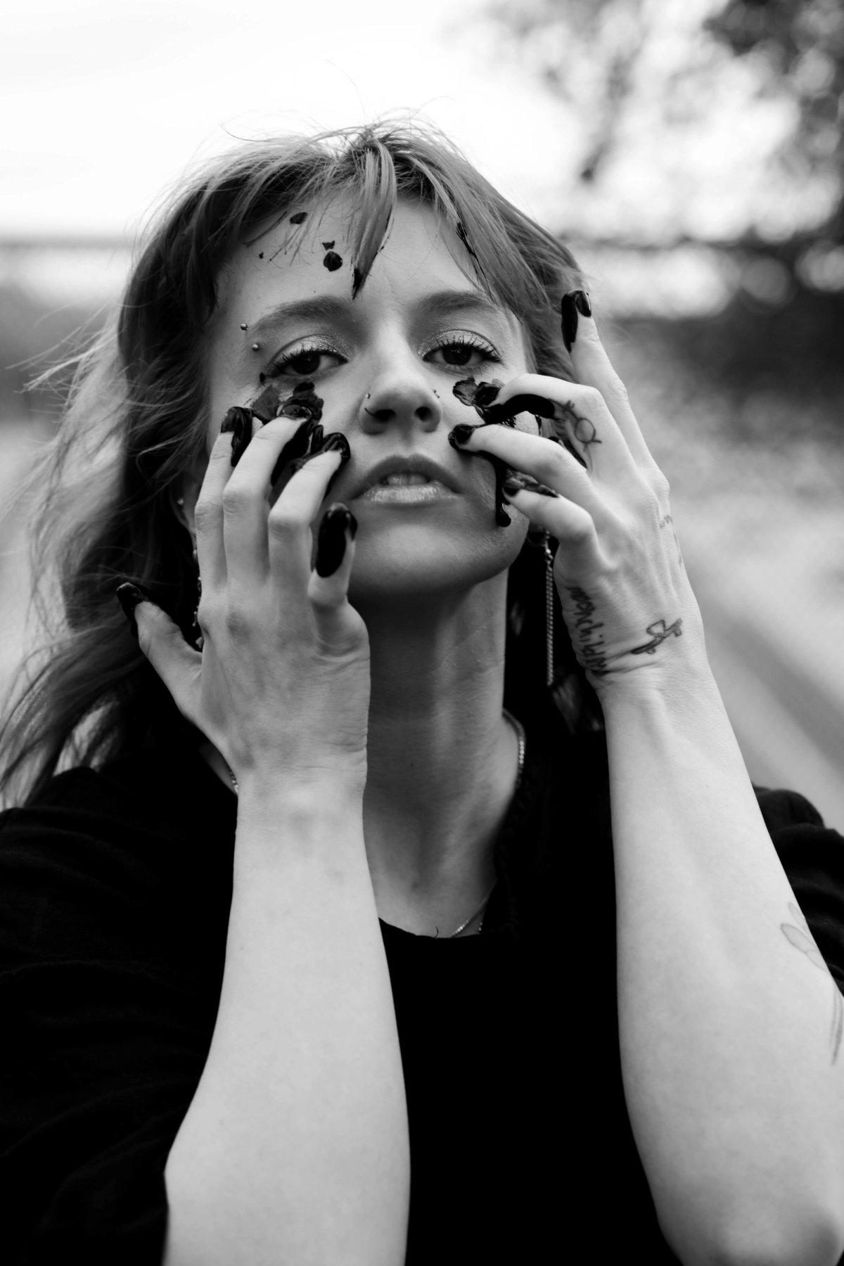 A woman looks straight at the camera with both paint-covered hands pressed to her cheeks.