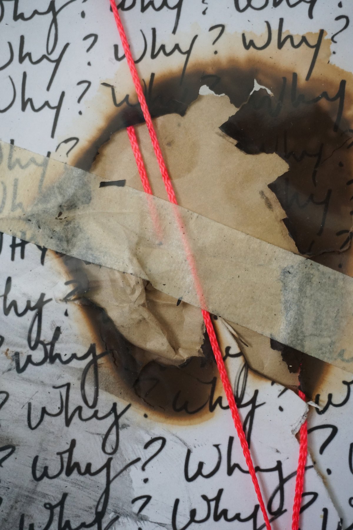 Detail: a burned hole in a 'Why?' page, patched with masking tape, red string running across.