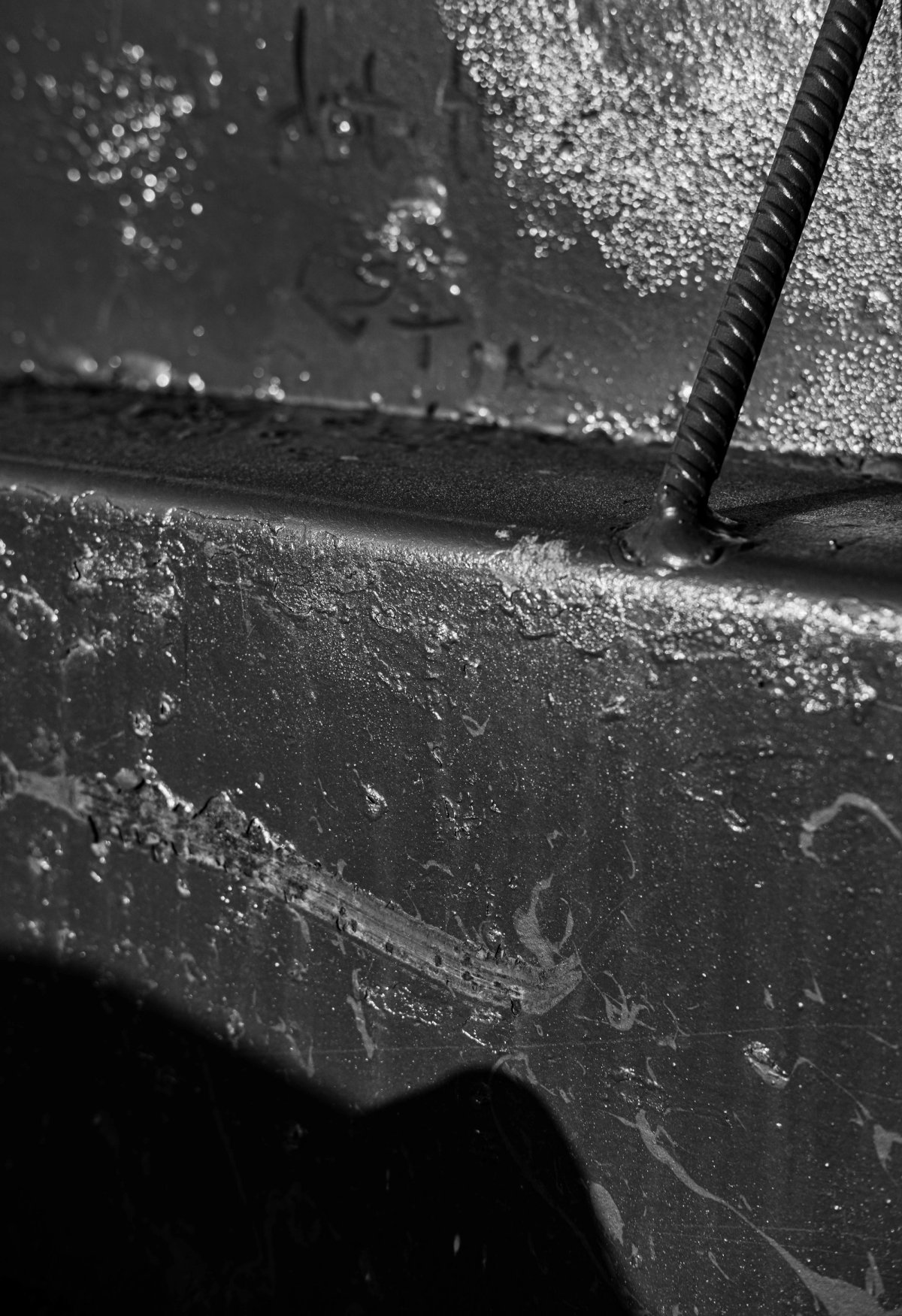 Wet, dark metal with a spiral rod rising from it, glistening with droplets.