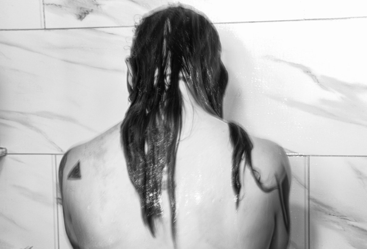 A woman seen from behind in a marble shower, wet hair down her bare back.