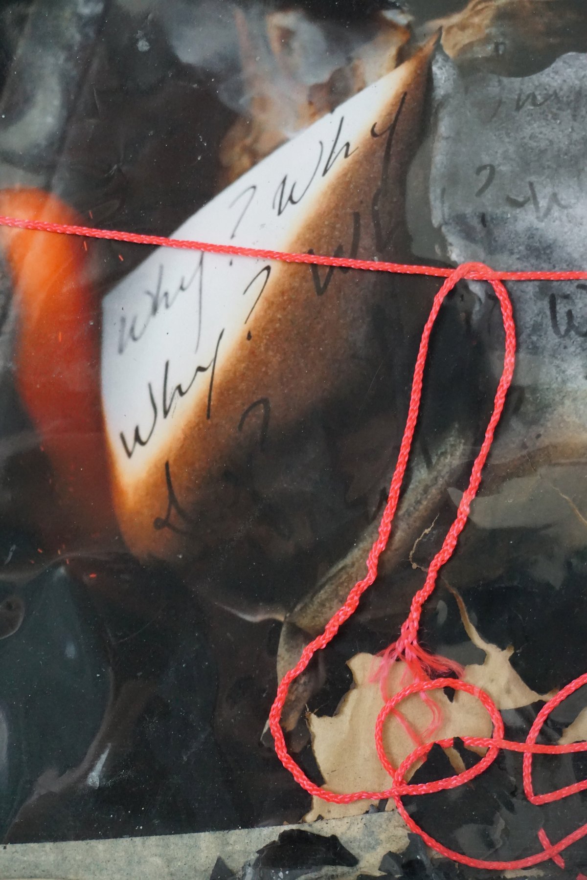 Detail: a curling page reading 'Why? Why?' glows orange at its burning edge, a red string tied across it.