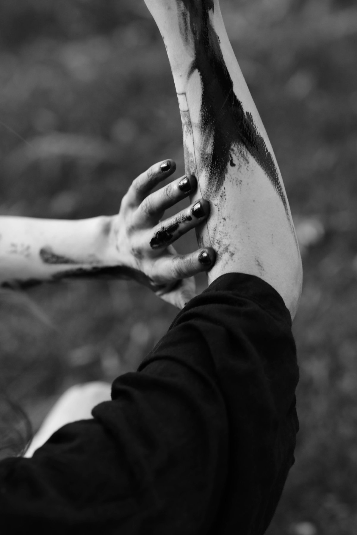 A paint-blackened hand grips a raised forearm streaked with black paint.