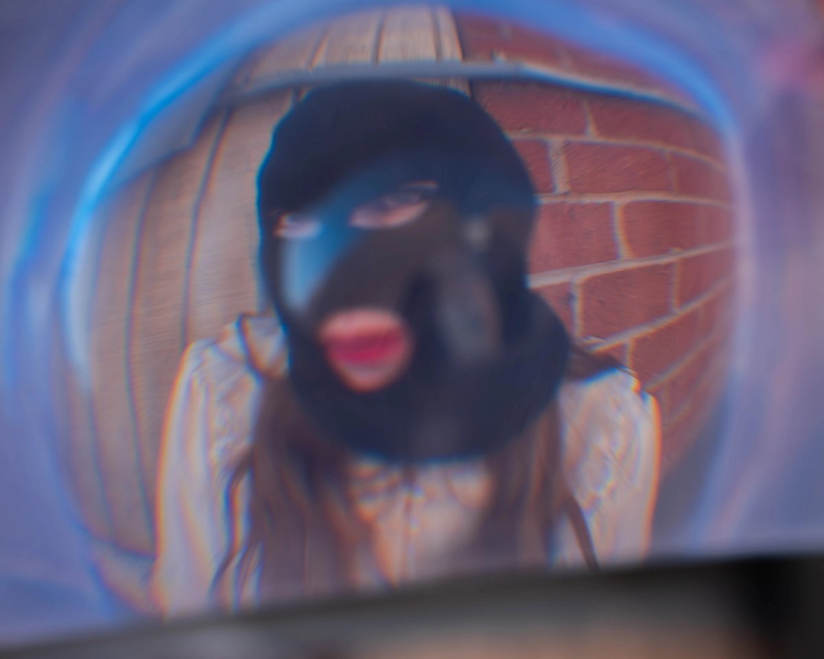 A masked face warped through a blue lens, lips bright red through the mouth hole.