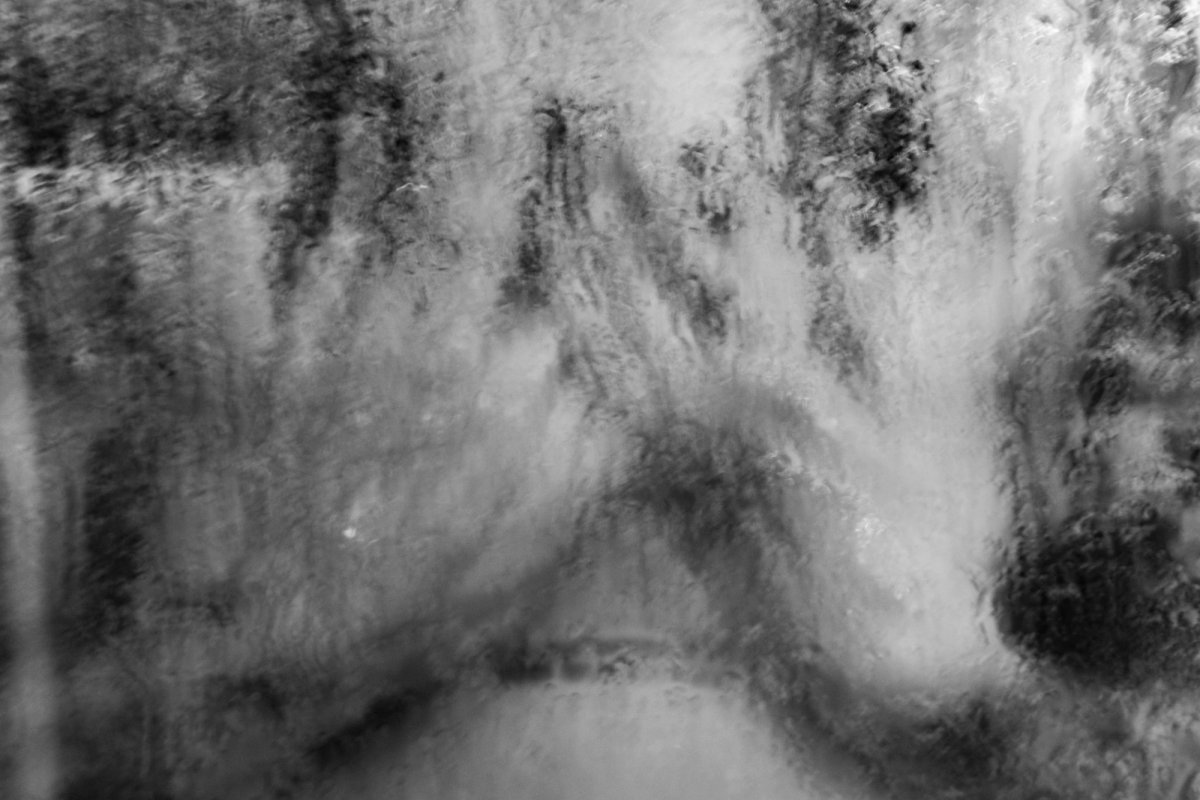 A dark, smeared texture of water and shadow, abstract and rough.