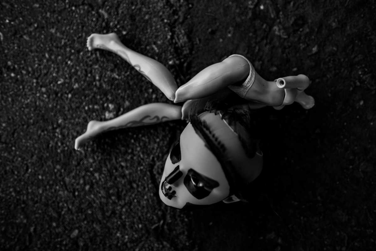 Seen from above, a doll with a skull face lies on asphalt, limbs bent in different directions.