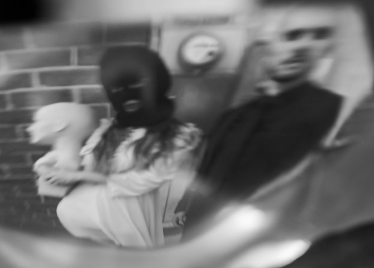 Through a warped lens, the masked woman and the man appear stretched and blurred together.
