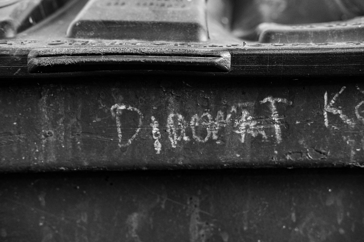 Close-up of a dark dumpster lid with words scratched into it in chalky white.