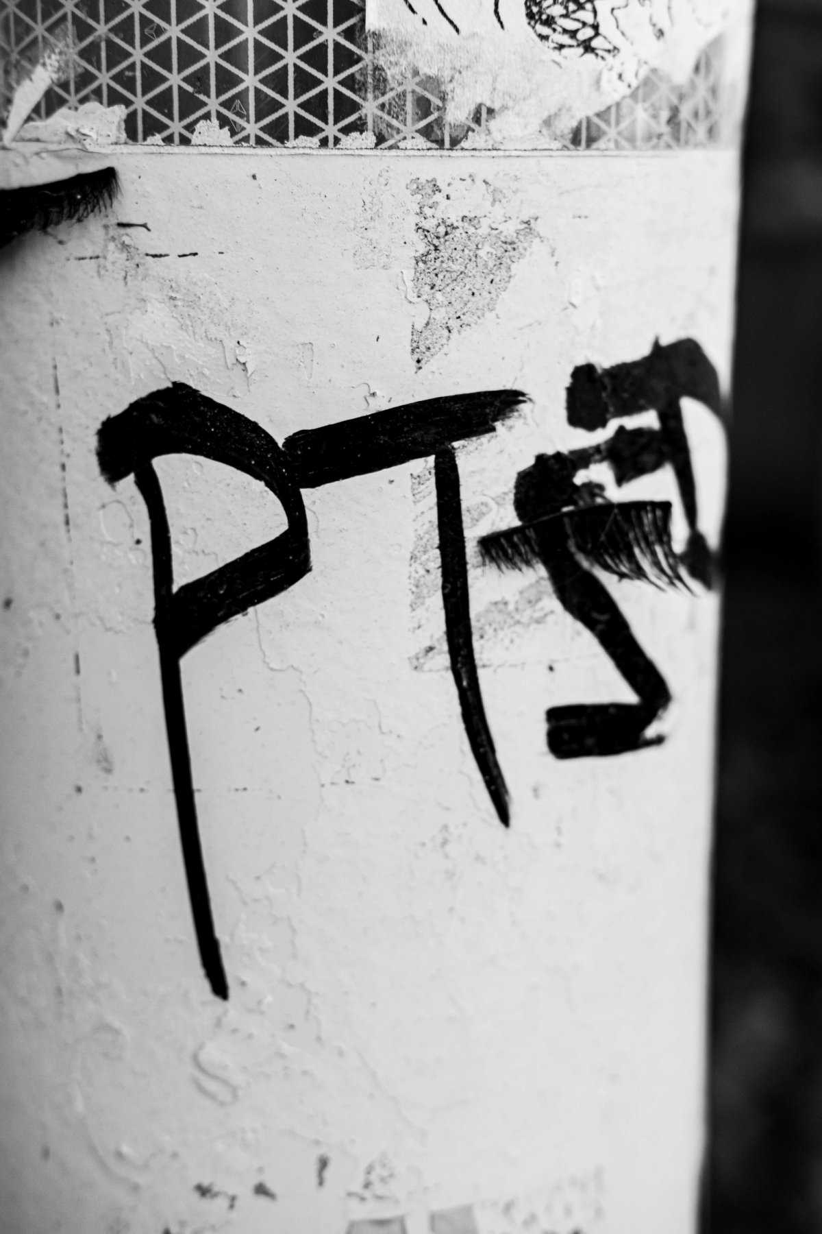 'PTSD' painted in thick black strokes on a white pole, with false eyelashes stuck to it.