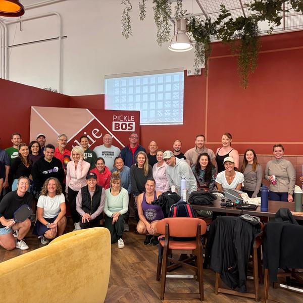 Large group posing in front of the pickleball signage.