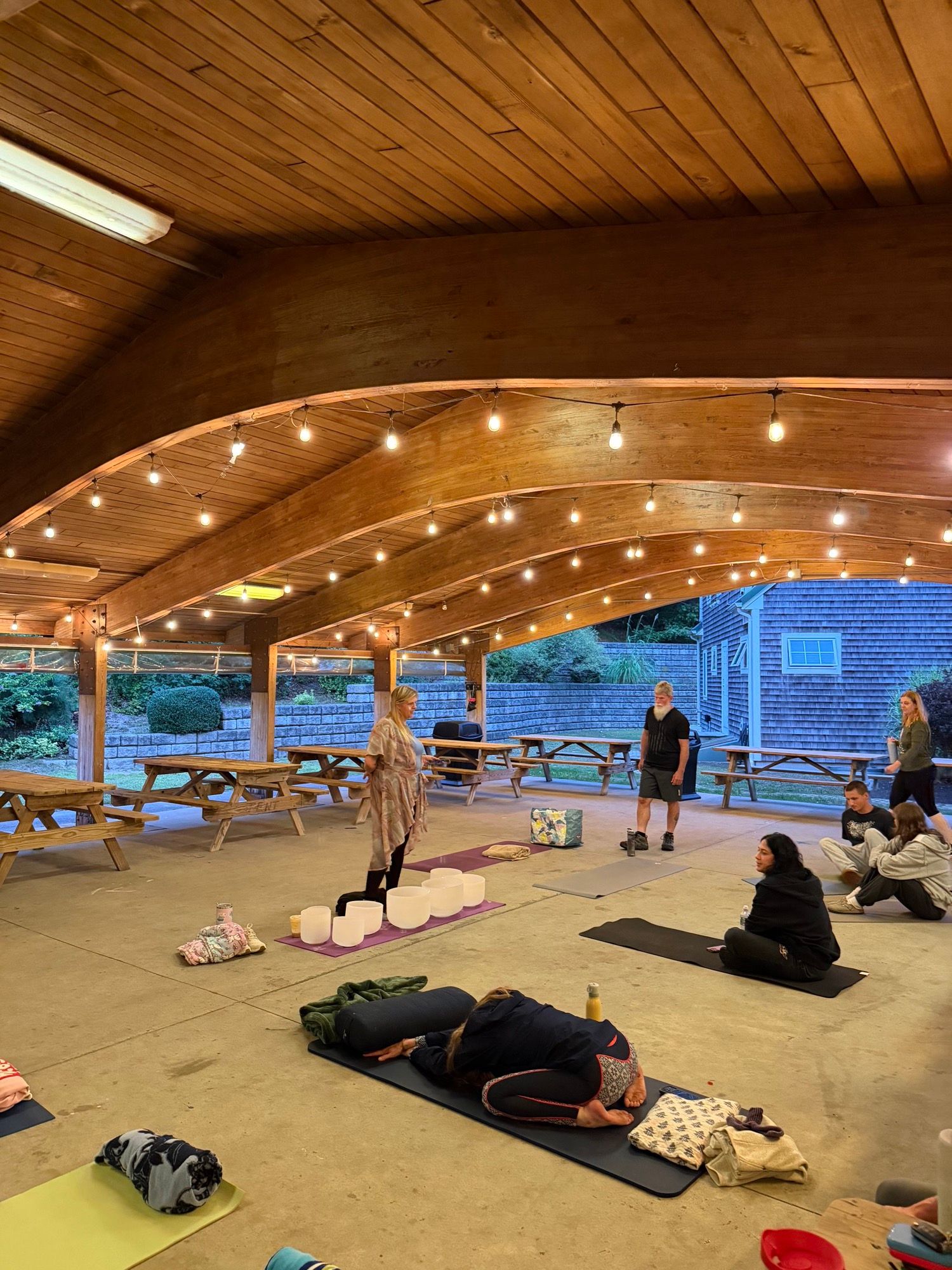 People settling onto mats and blankets under the pavilion’s vaulted wooden ceiling as the session begins.