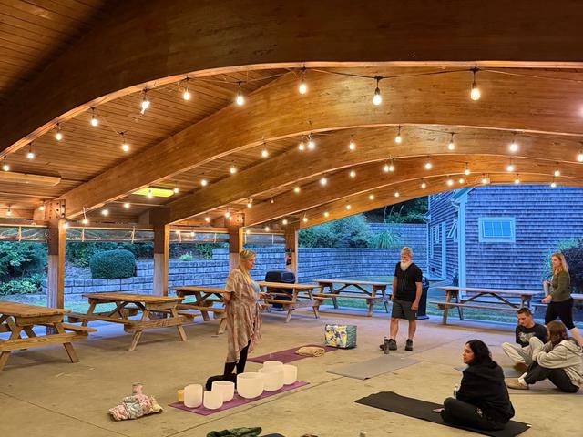 People settling onto mats and blankets under the pavilion’s vaulted wooden ceiling as the session begins.