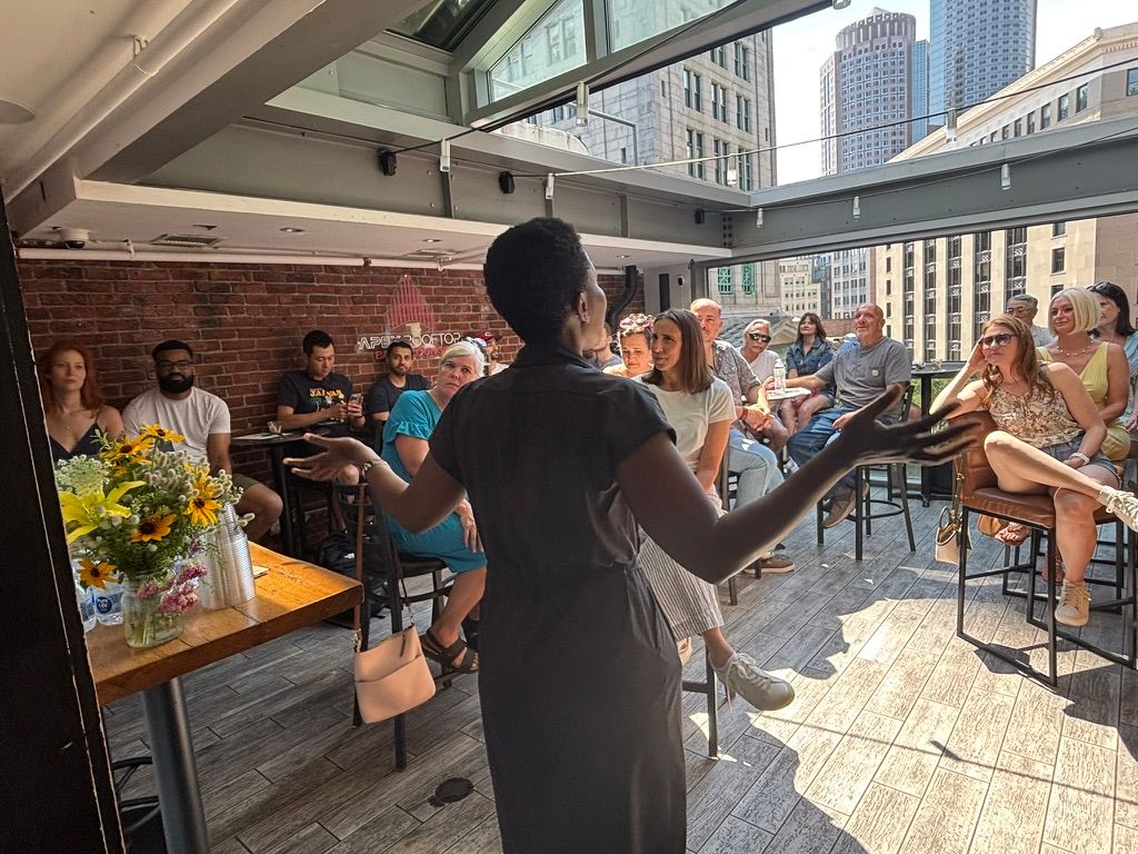 A woman addressing a crowd of seated guests at a coffee tasting.