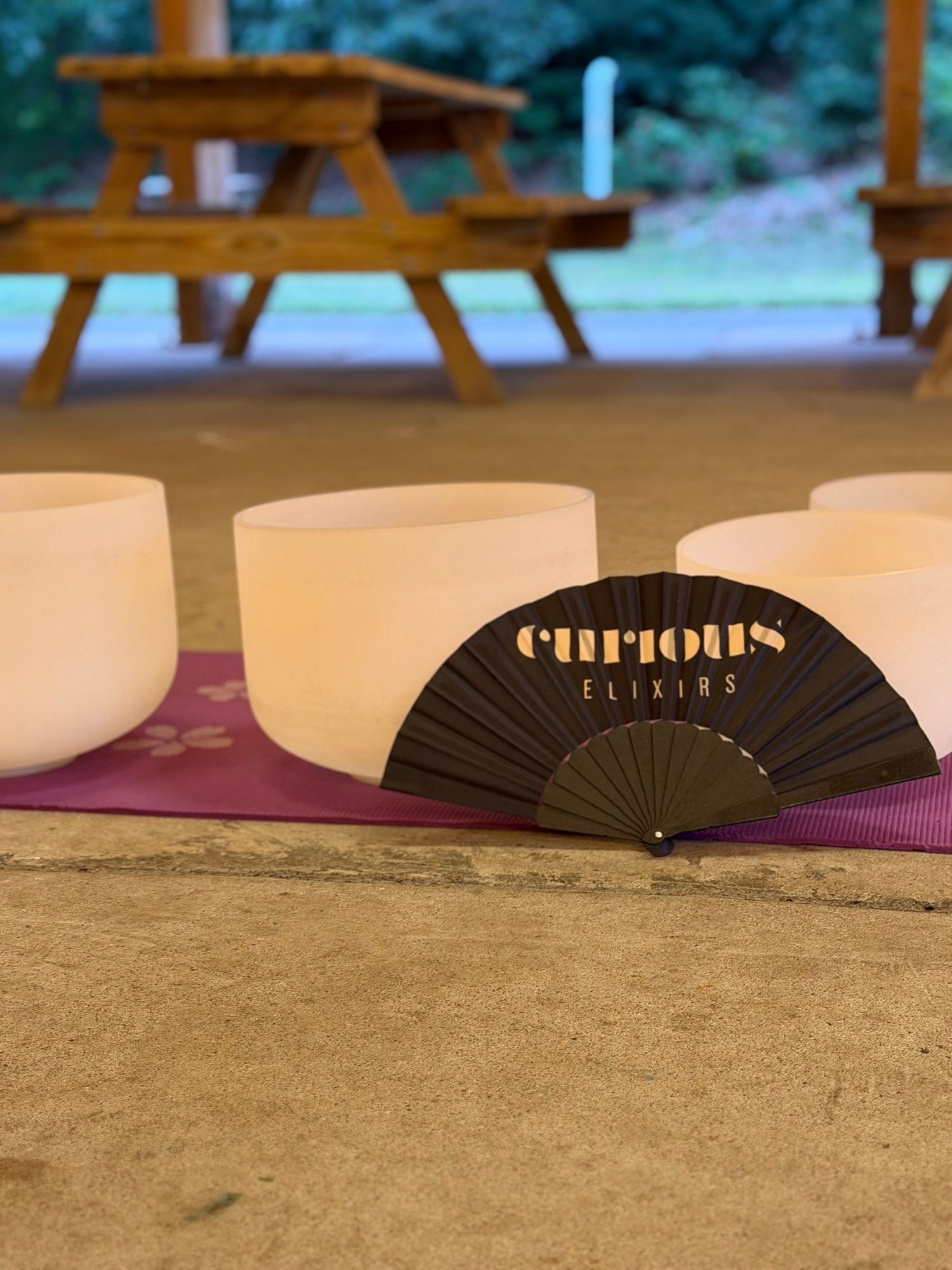 A row of frosted crystal singing bowls on a purple mat, with a folding fan propped among them.