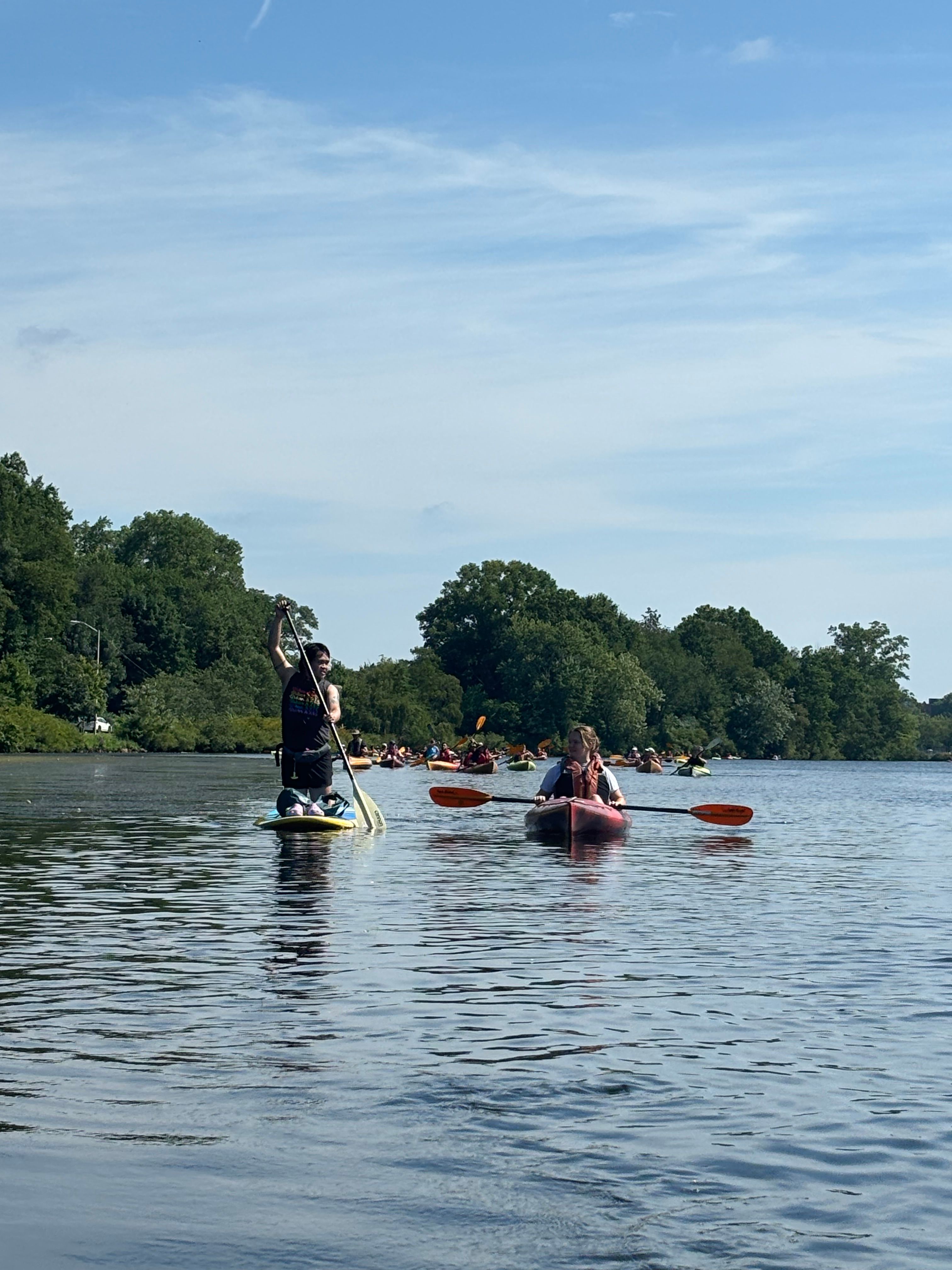 Man kneeling on a paddle board next to woman in kayak.