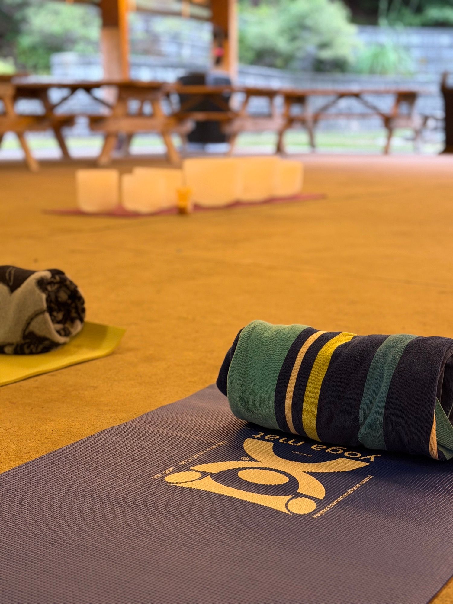 A rolled striped blanket on a yoga mat laid out on the pavilion floor, singing bowls glowing behind it.