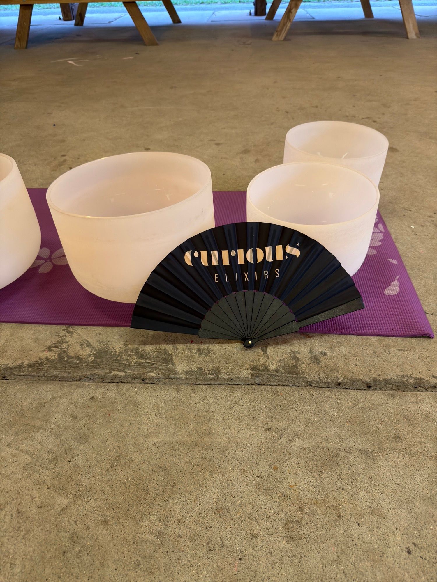 Three crystal singing bowls arranged on a purple mat on the pavilion floor, picnic tables behind.