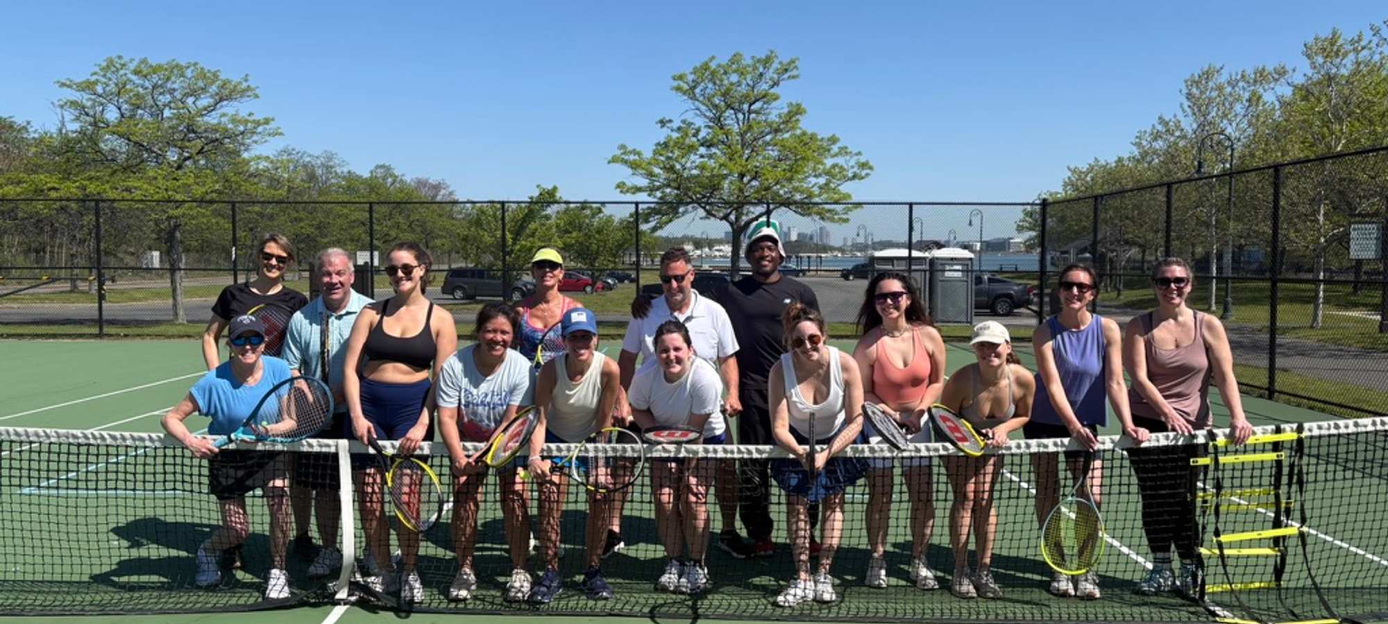 Members leaning against the net of a tennis court after a clinic.