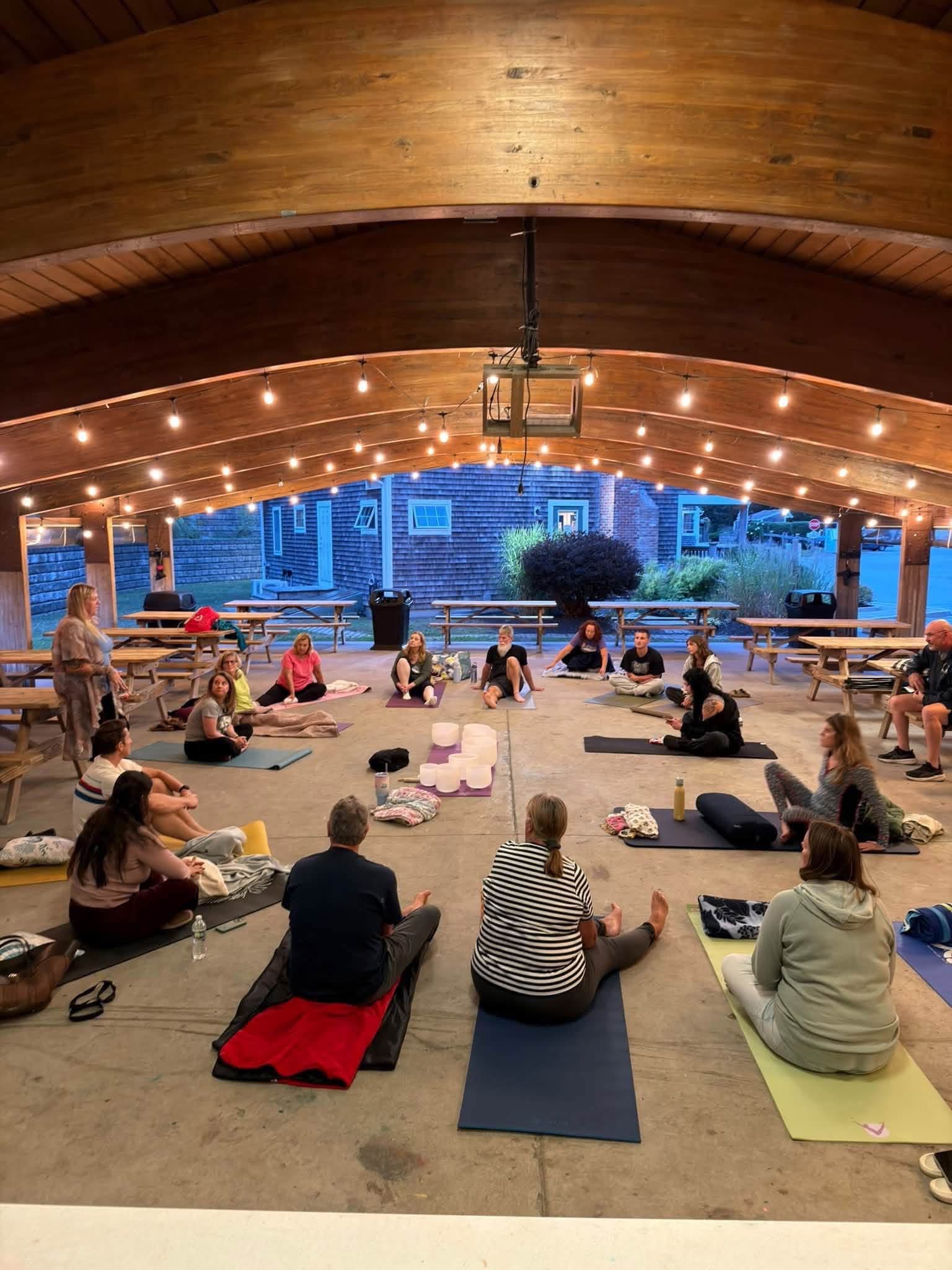 A seated group at a sound healing event outdoors under lights.