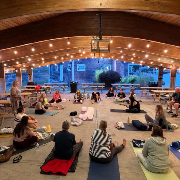 A seated group at a sound healing event outdoors under lights.