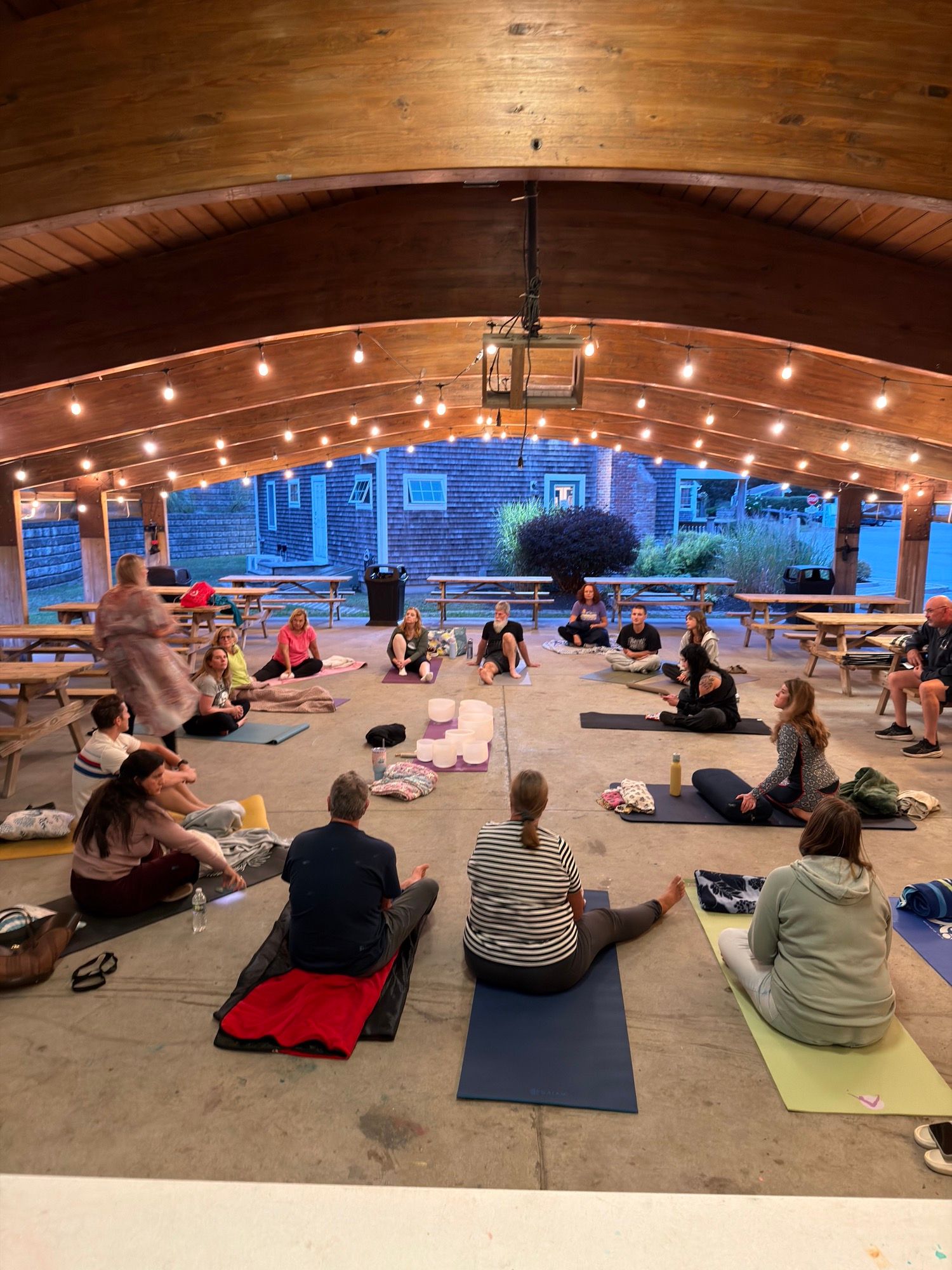 The group sitting and lying on mats and blankets spread across the pavilion floor before the sound bath.