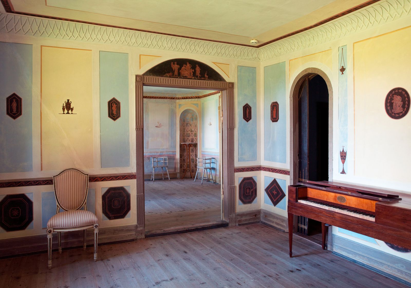 Det pompejanske værelse i Det Norske Hus ved Liselund med antikinspirerede vægdekorationer, et fortepiano og udsigt til tilstødende stue.