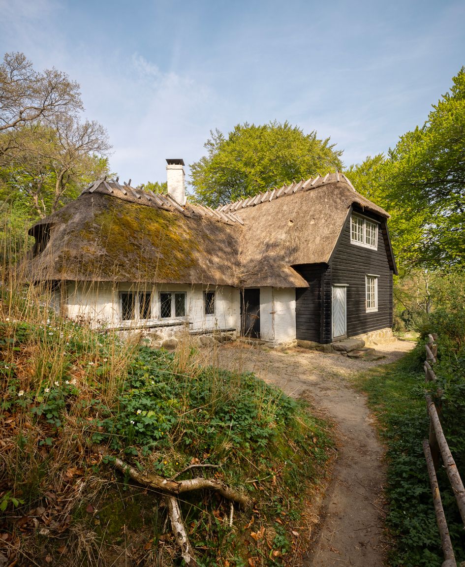 Det Norske Hus i Liselund Park set udefra – en langstrakt bygning i bindingsværk og mørkbejdset træ med stråtag.