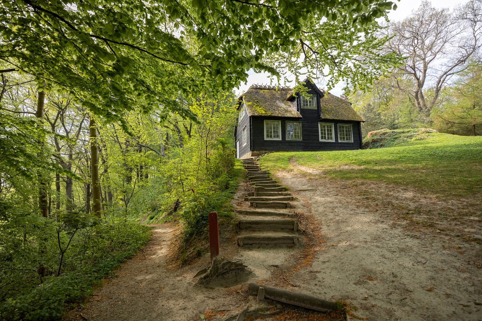Det Norske Hus i Liselund Park, en lille mørk træbygning med græstag, nået via en trappe gennem skoven.
