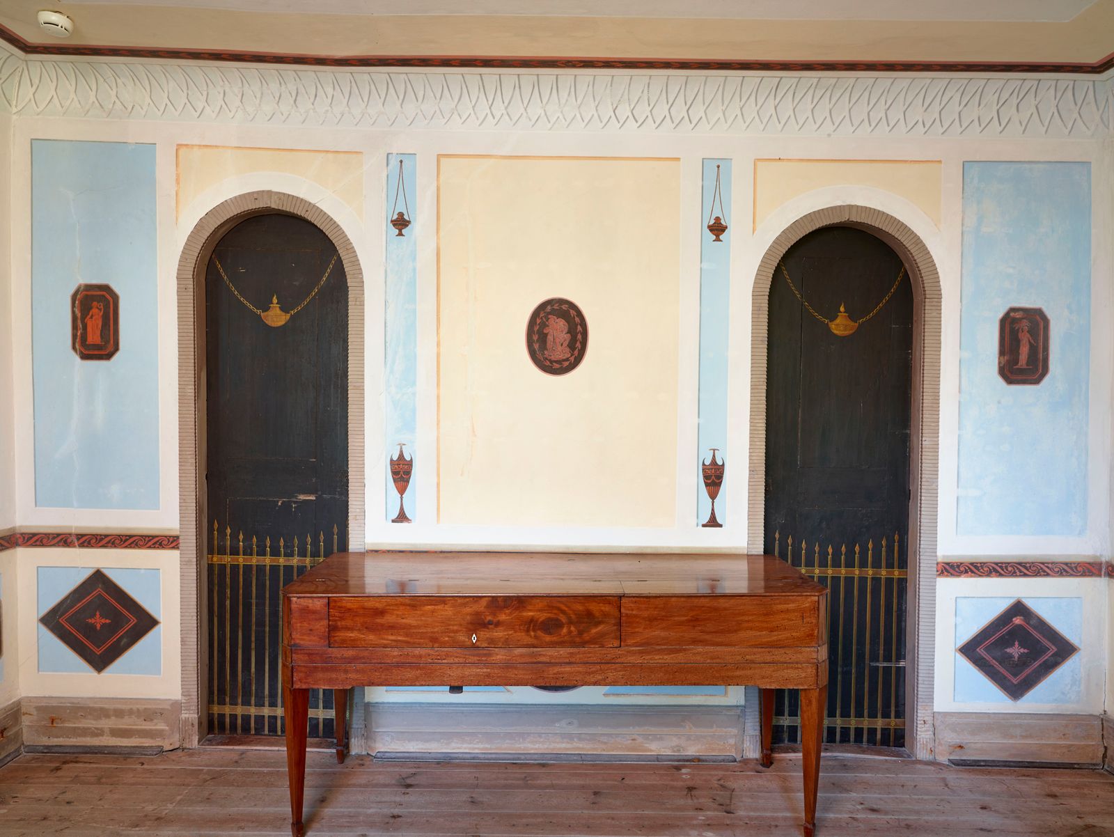 Det pompejanske værelse i Det Norske Hus ved Liselund med malede antikmotiver, buede døråbninger og et antikt bord.