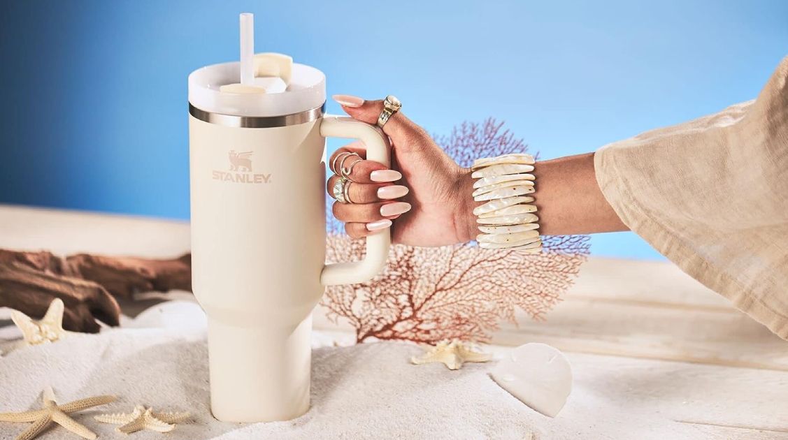 Person holding a Stanley Quencher with a beach-themed background