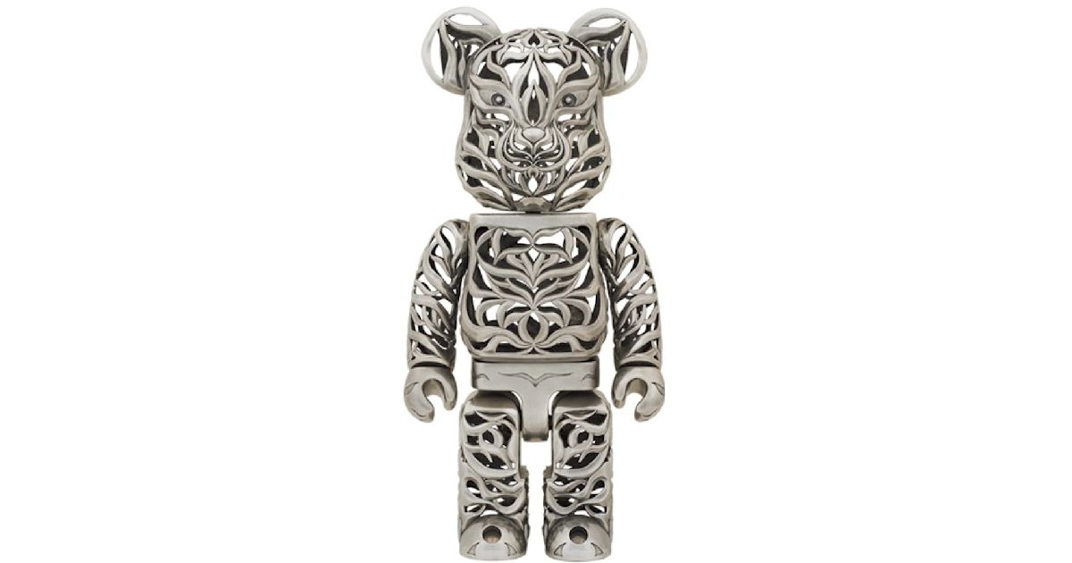 A silver Bearbrick with a cutout pattern all over and a tiger-like face.